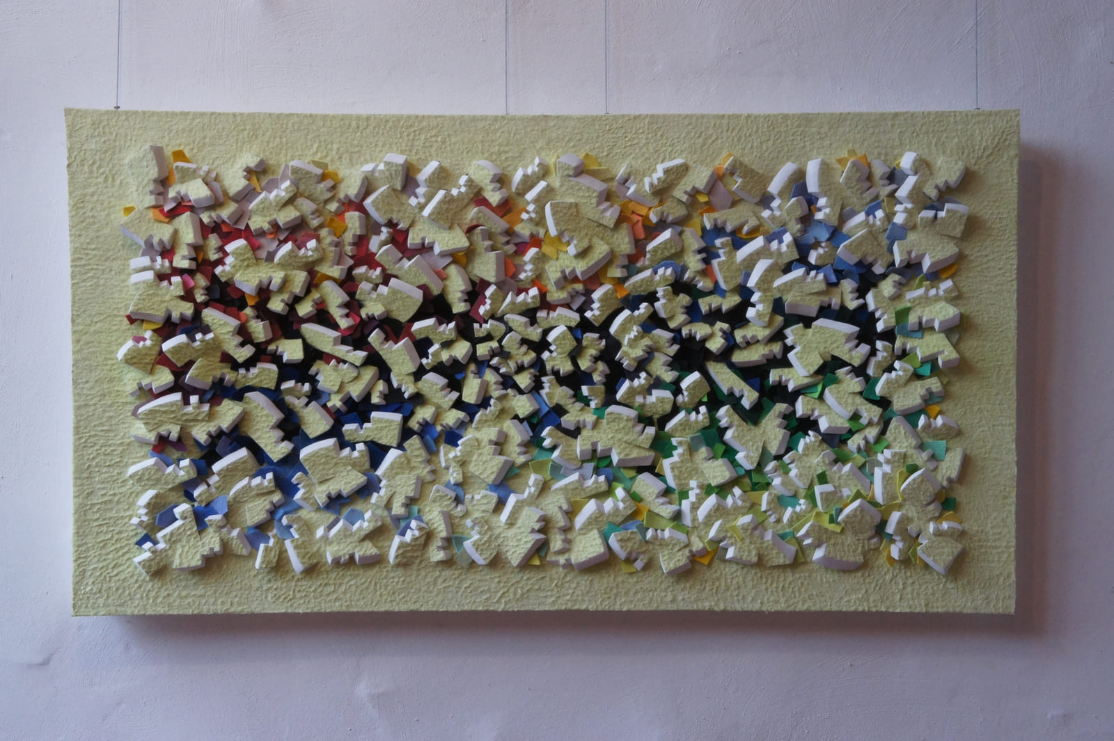 Dichtes gelbes Relief mit farbigen Zwischenlagen an einer weißen Wand.